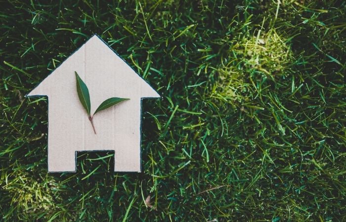 Représentation écologique d'une maison positive avec une silhouette en bois et une feuille verte, symbolisant le respect de l'environnement et l'énergie renouvelable.